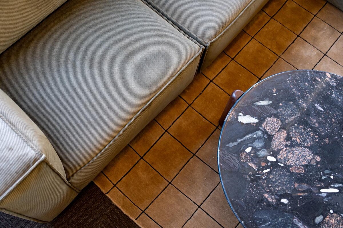 Close-up of a textured stone coffee table and taupe sofa on a grid-patterned tan rug.