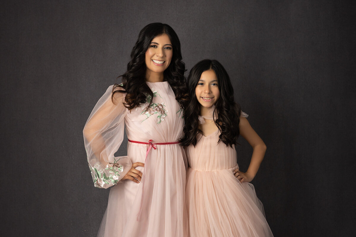 A Dallas family photographer captures a beautiful mother and daughter in matching dresses, both smiling brightly against a dark backdrop.