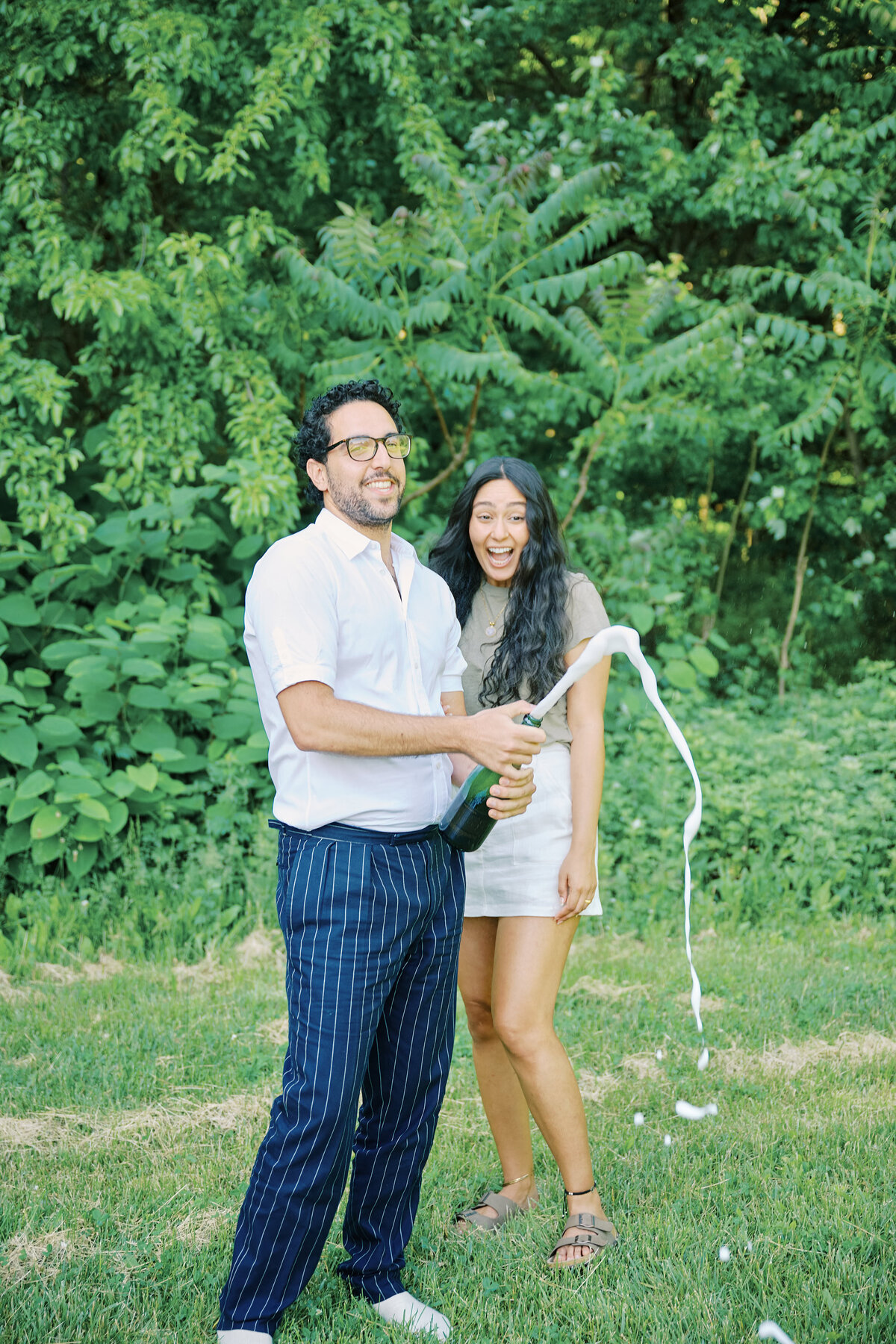 A couple pop champagne after a successful New York City Picnic Proposal, photo taken by NYC Proposal Photographer, Corey Lamar Photography