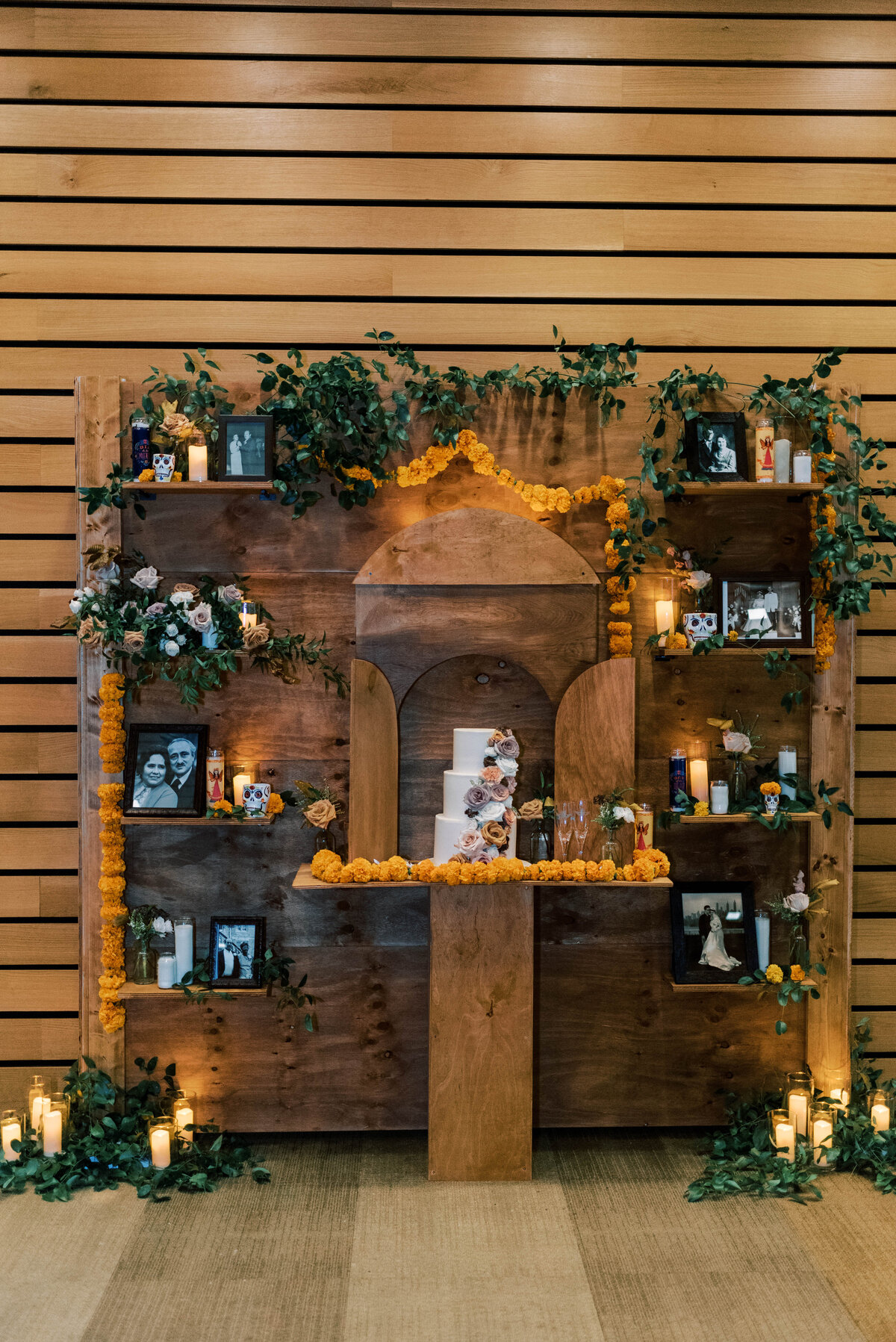 Wooden wedding backdrop design with wedding cake, photos, and greenery