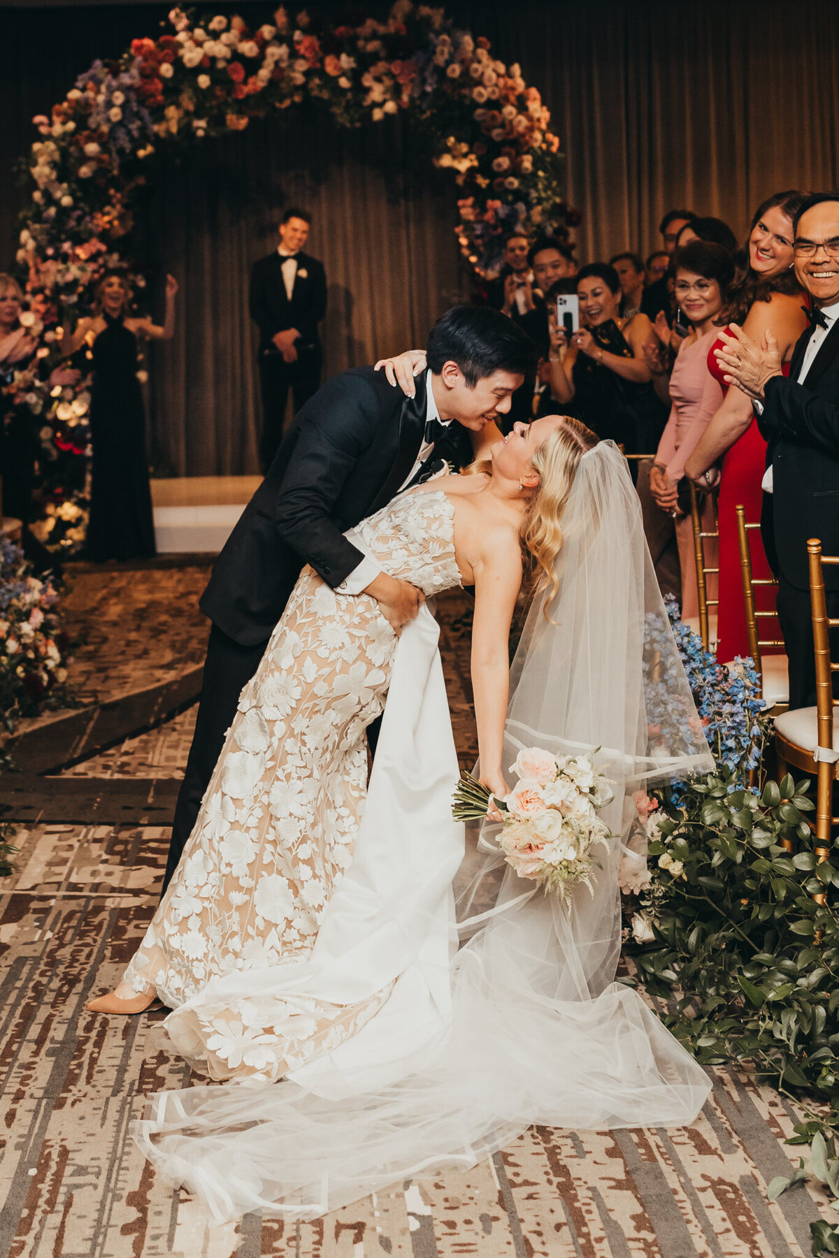 groom dips his wife for a kiss while crowd cheers