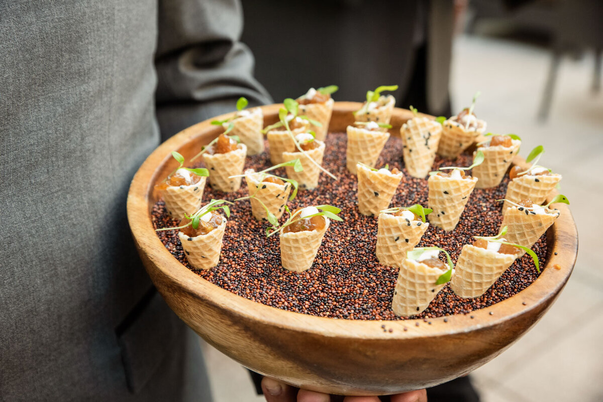A person is holding a wooden bowl filled with waffle cones filled with food