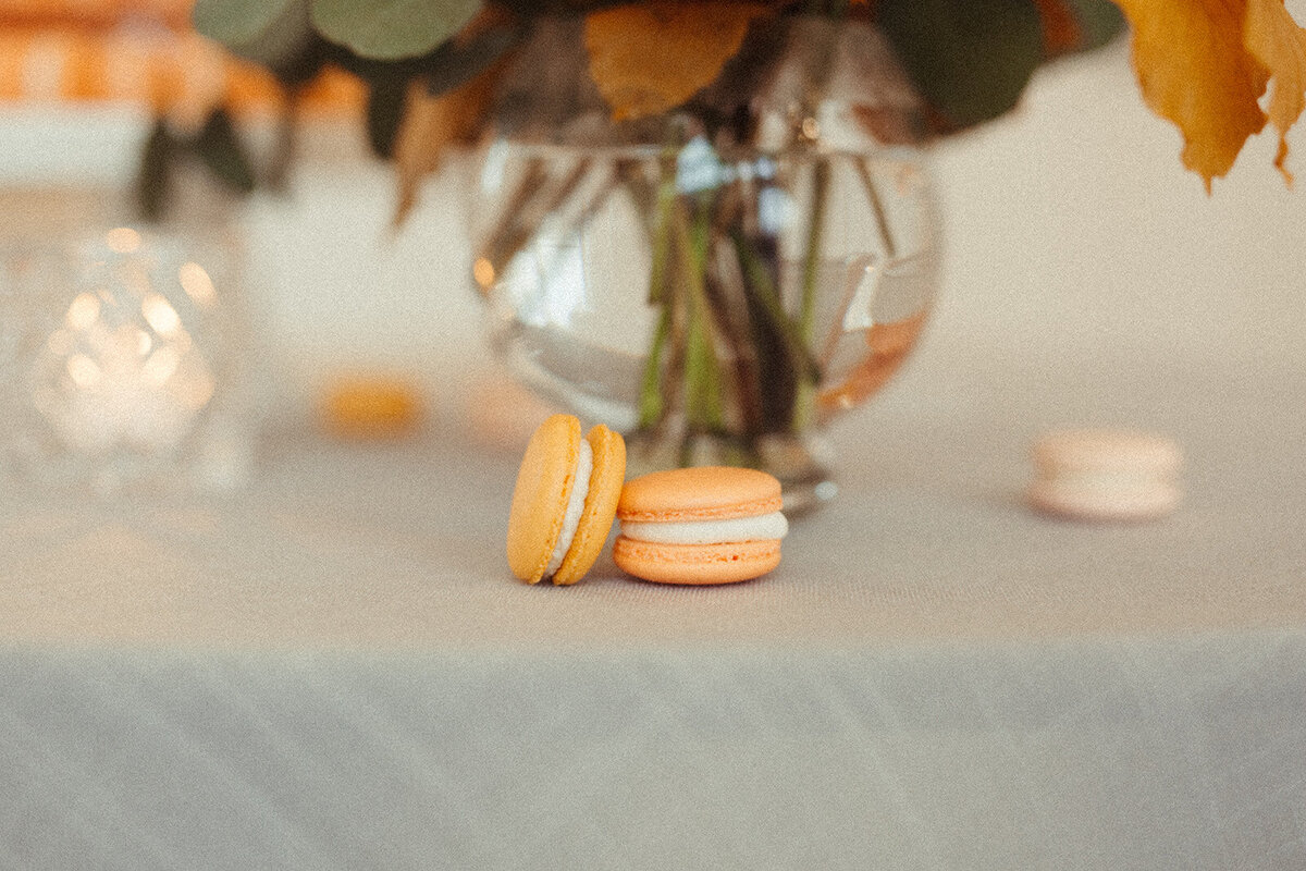 Peach and blush macaroons with a vase filled with water and flowers atop a table with gray linen.