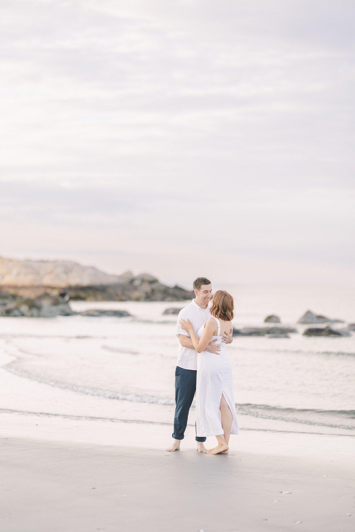 A couple dancing on the beach with rocks in the background during their Wingaersheek Beach engagement session