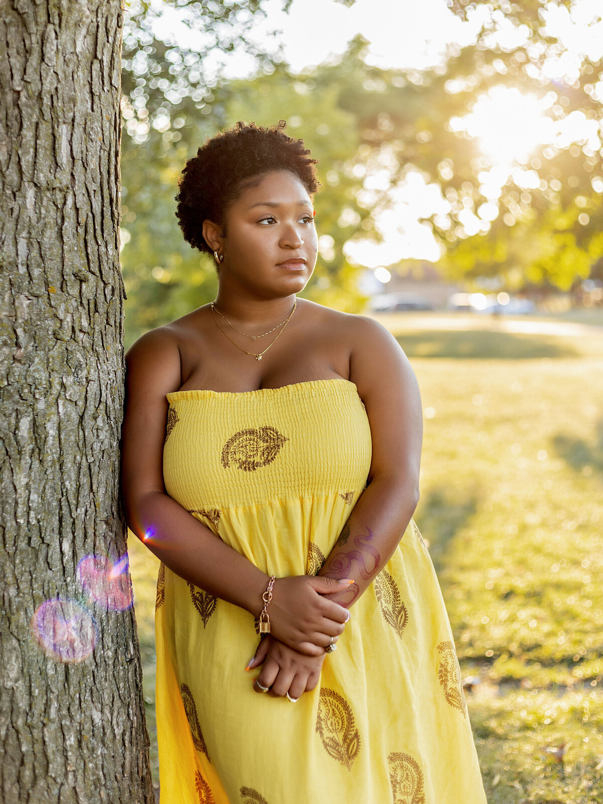 Woman in yellow halter sundress leaning on tree at sunset