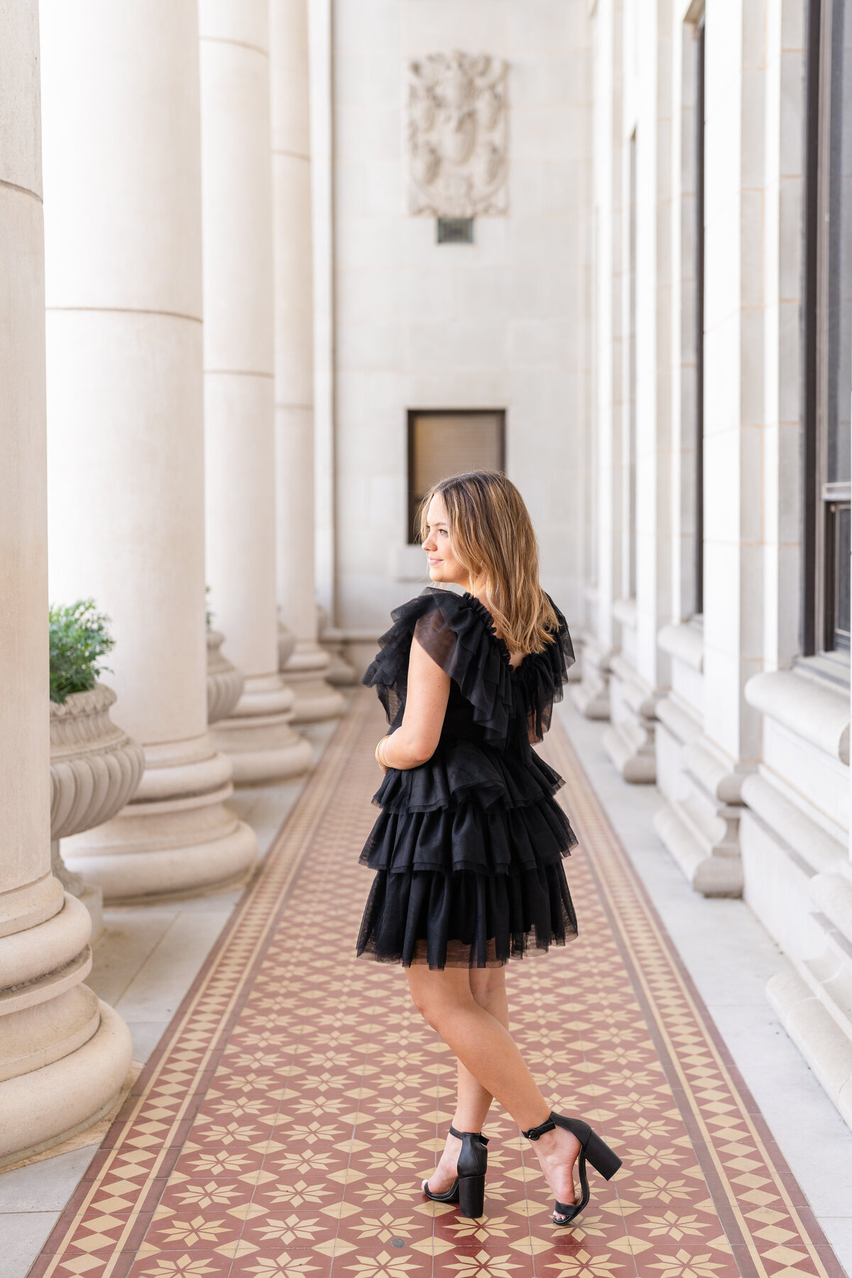 Texas A&M senior girl turned away from camera and looking over shoulder while wearing fluffy black dress in middle of Administration Building columns