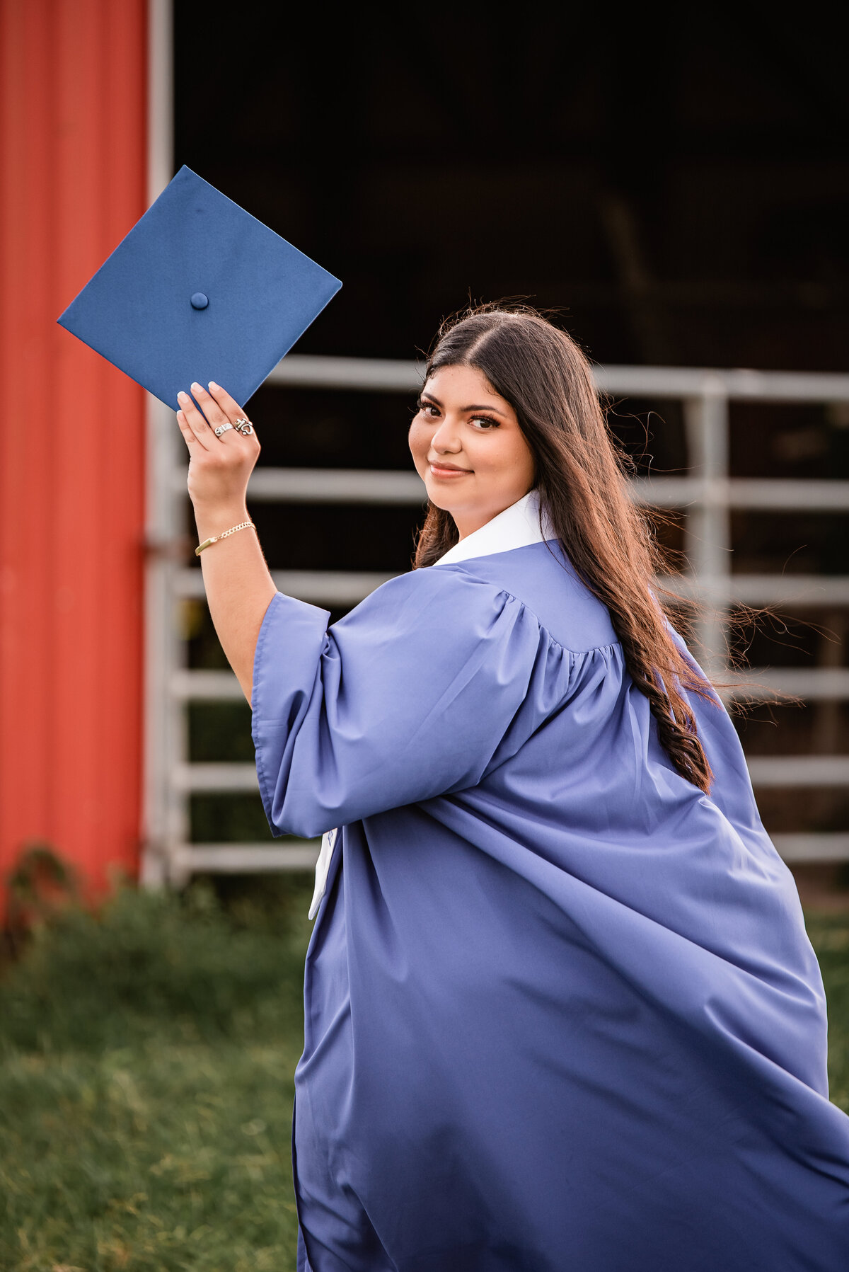 A Chavez High School senior looks over her shoulder and shows off her cap while standing in front of a red barn.