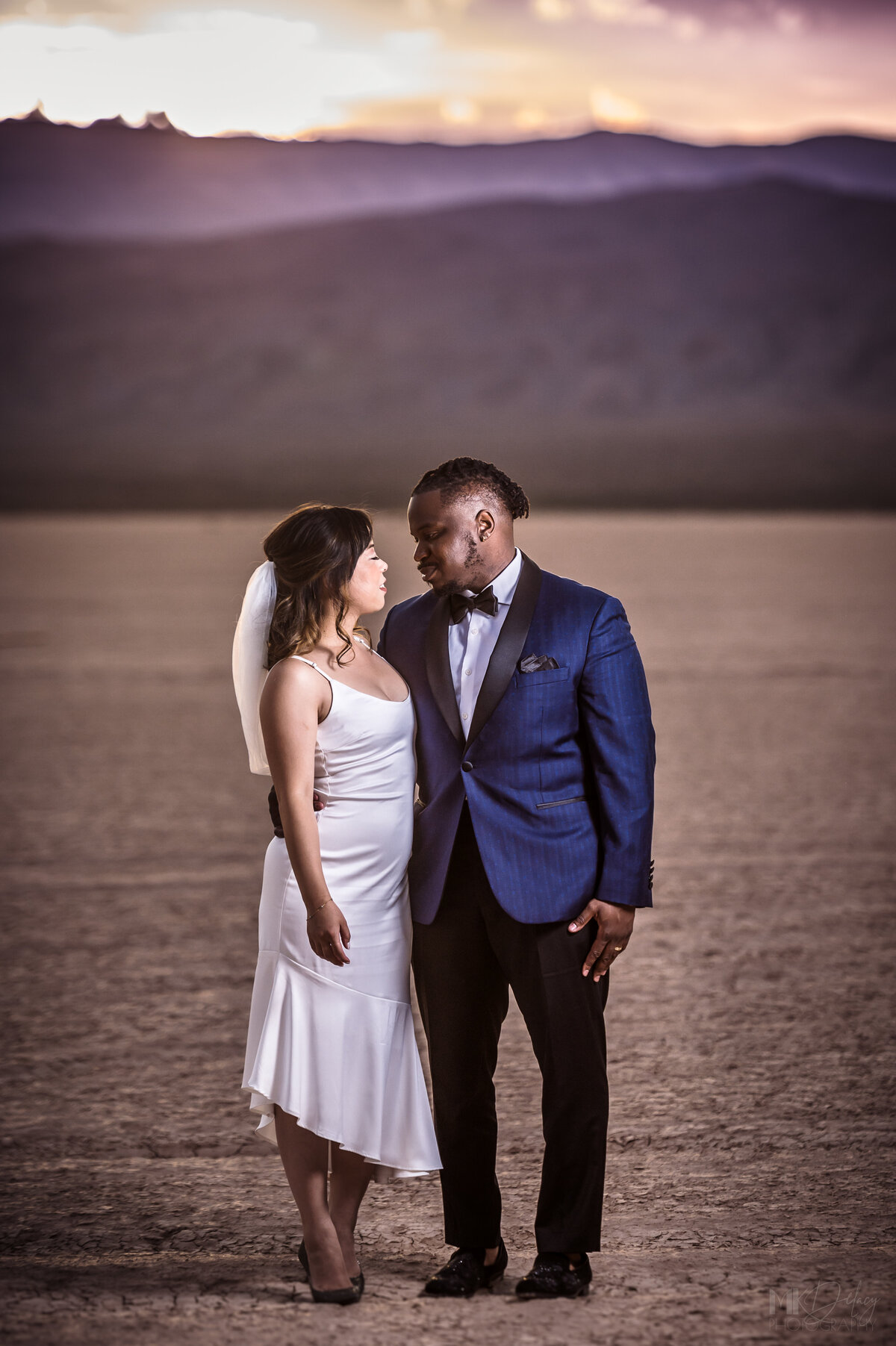 Martha Stewart weddings  couple GQ style couple bride and groom stare passionately at each other  las vegas elopement on the dry lake bed  at golden hour groom in blue suit jacket and black  pants  las vegas elopement eloping in vegas  las vegas wedding photographers las vegas wedding photography mk delacy photography