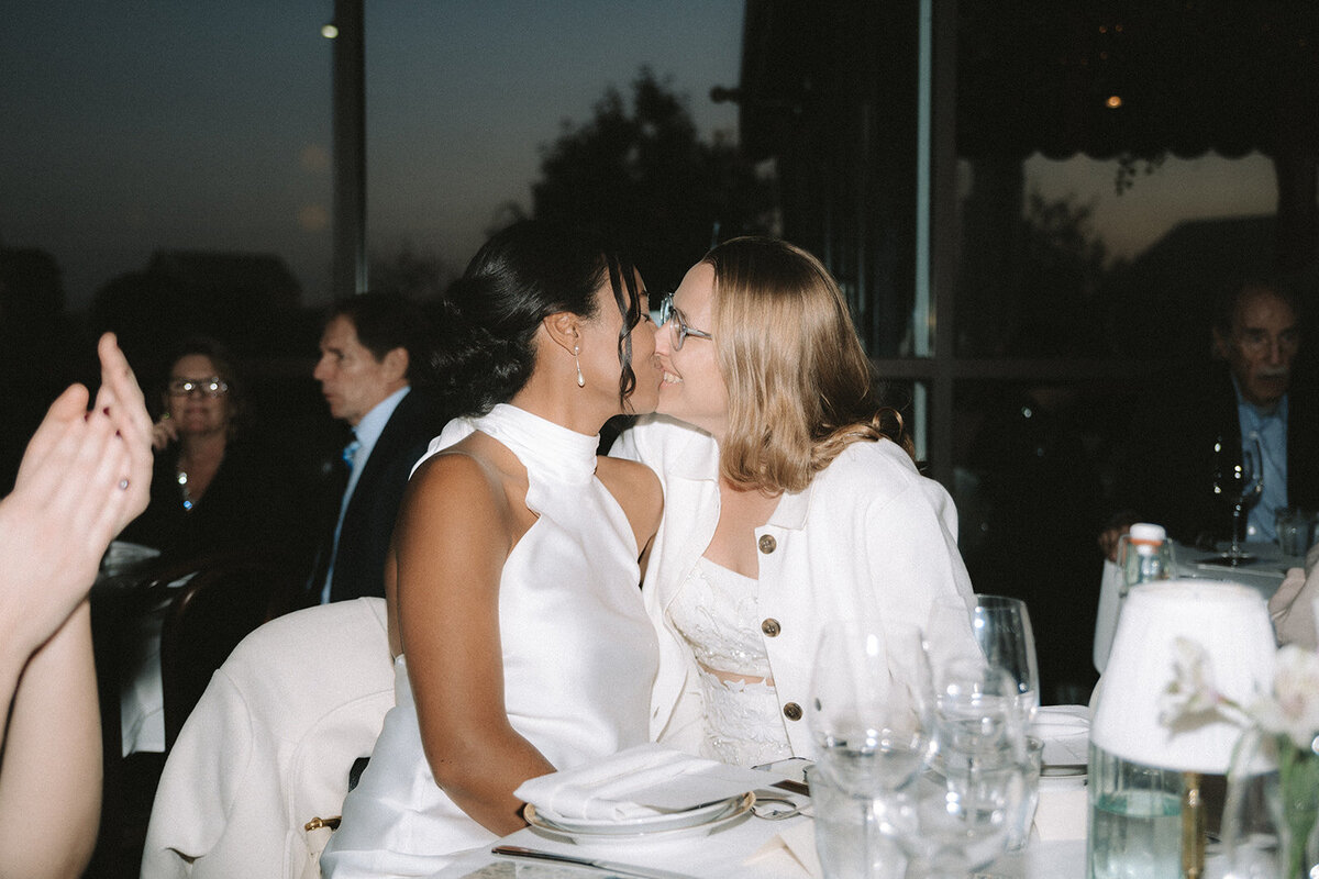 Two brides sharing a kiss inside of their restaurant reception