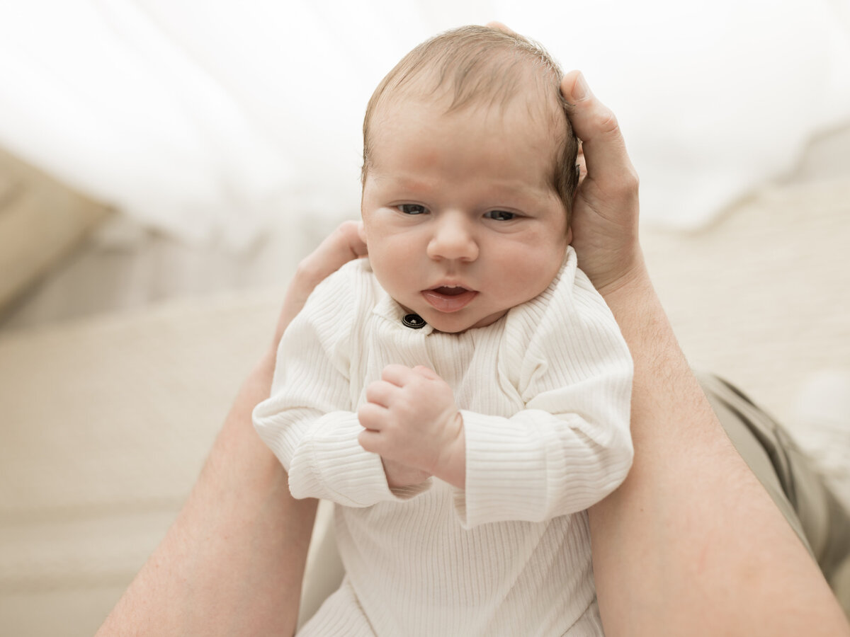dad holding newborn baby boy in white onesie for studio photoshoot 