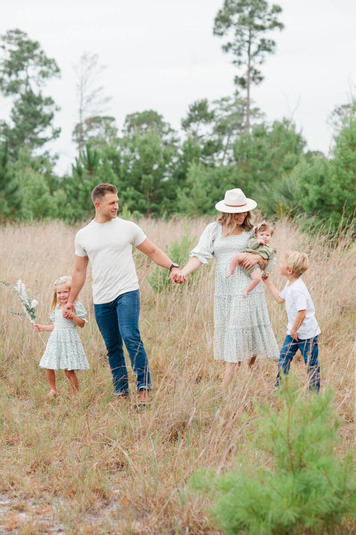 Family holding hands and walking through a tall grass field during their Orlando family photography session