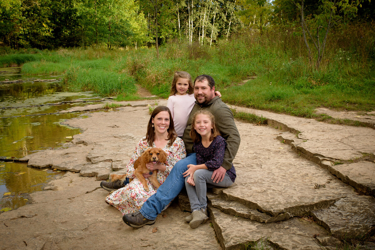 Family portrait with Mom, Dad, two little girls and their small dog sitting along the banks of a creek at Fonferek Glen County Park near Green Bay, Wisconsin.