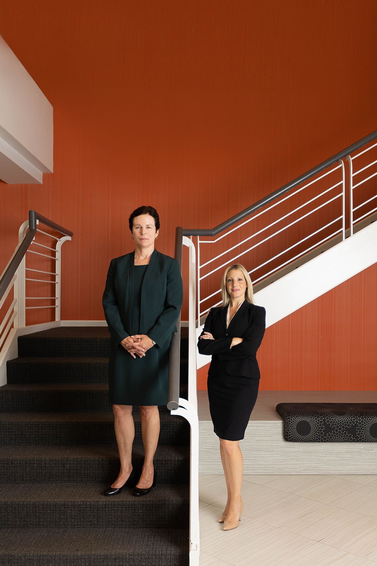 Two well dressed businesswomen standing in an orange stairwell