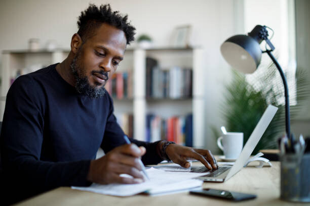 Hands of Black person writing and typing on computer