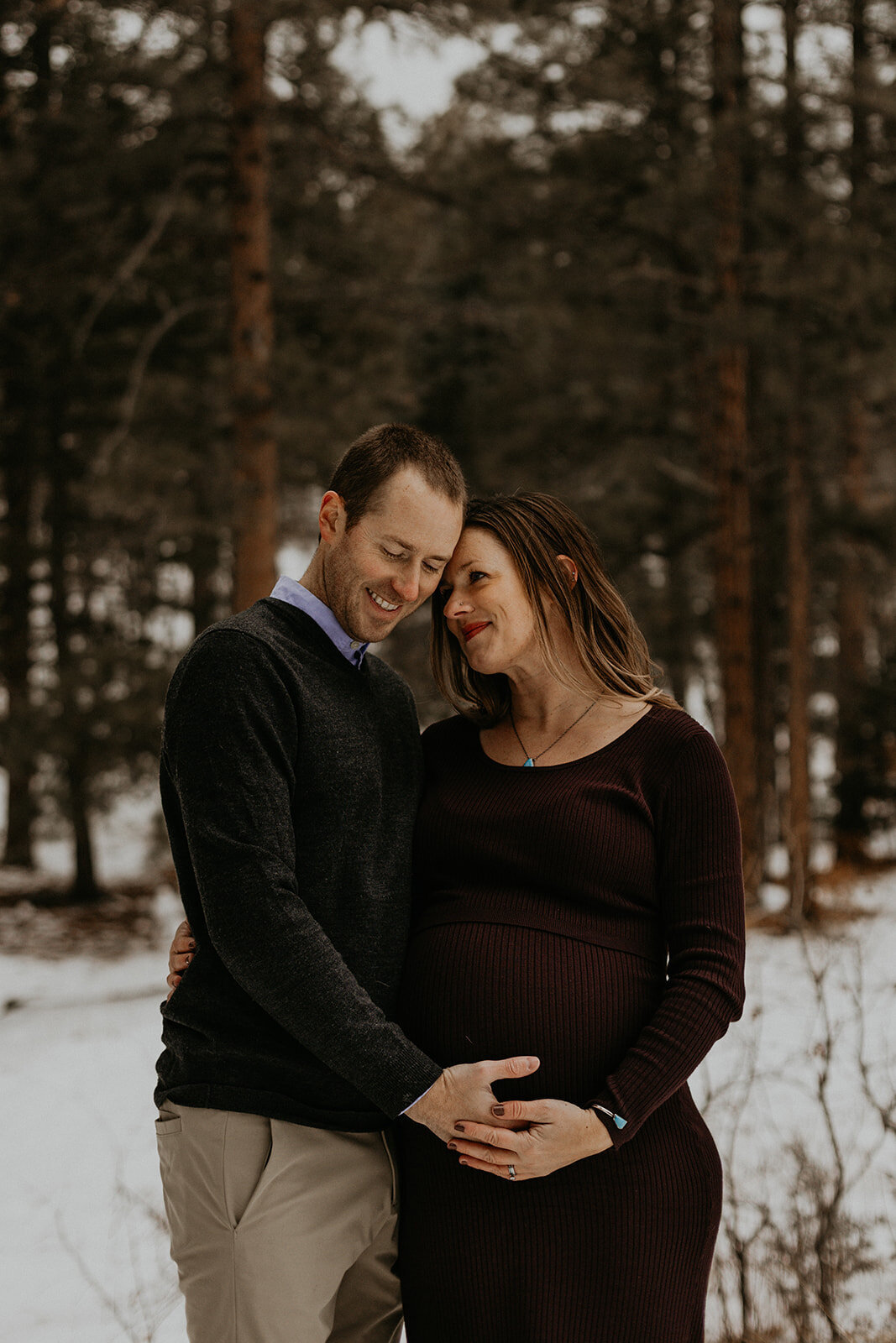 married couple hugging and holding her pregnant belly in the snow