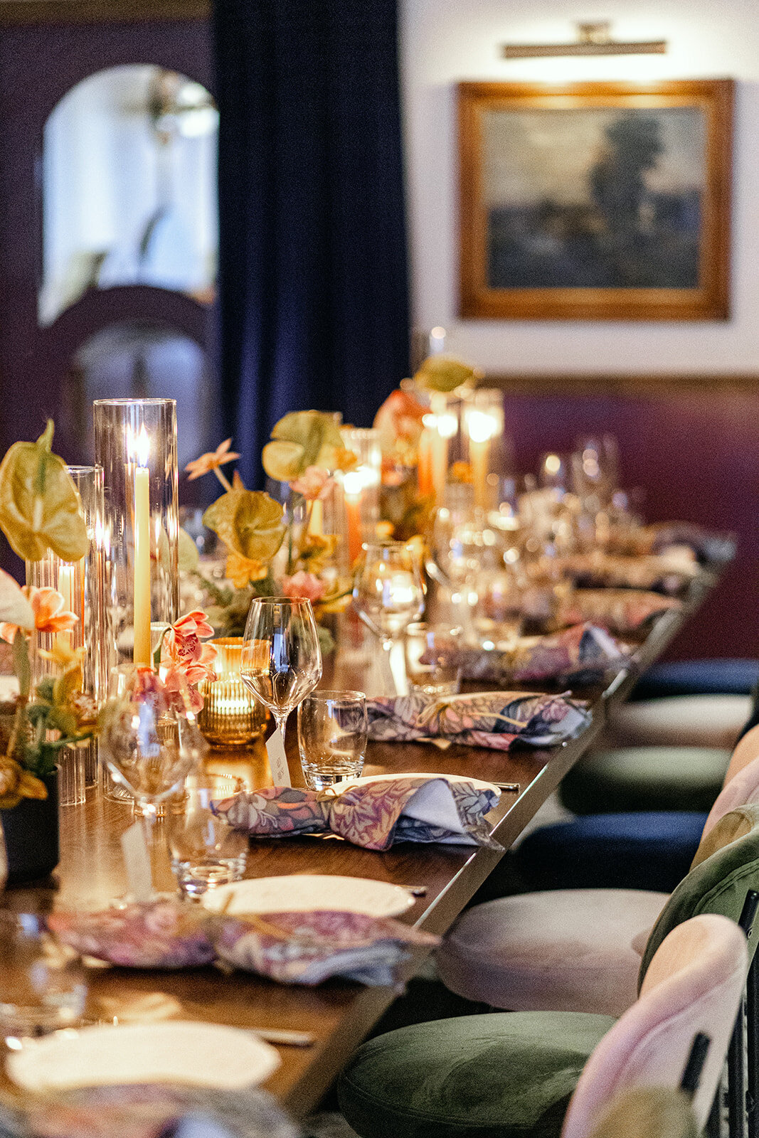 Long dining table adorned with golden-hued flowers, tall candles, and deep burgundy table settings