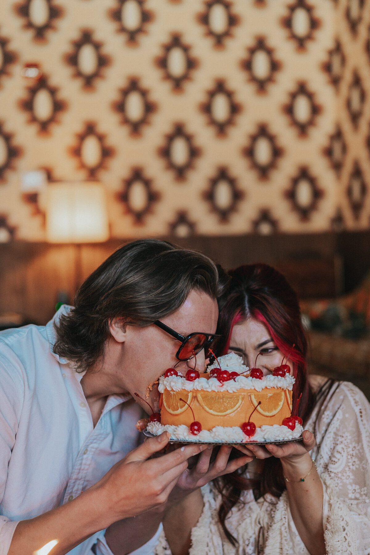 A couple stuffs their face into their bright orange elopement cake