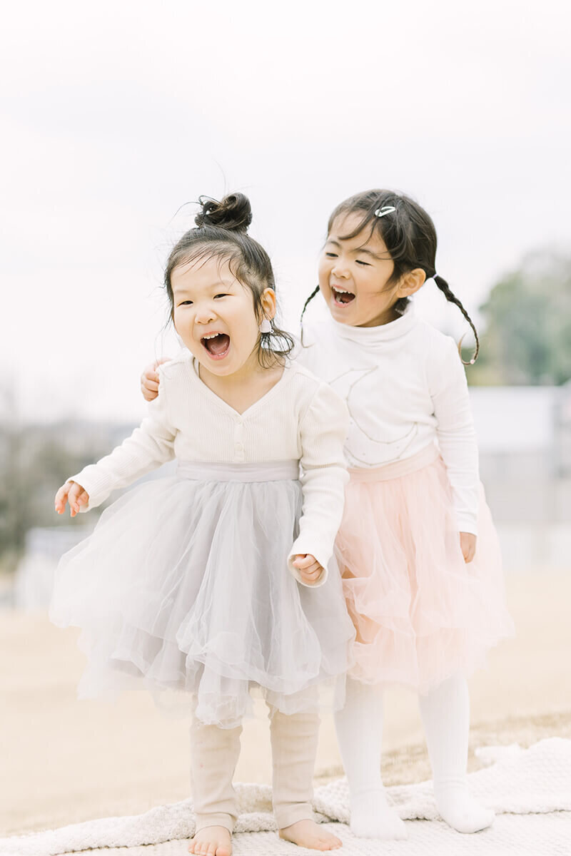 ブルーとピンクのチュールスカートをはいた可愛らしい3歳の女の子2人が笑って楽しそうにしている可愛らしく美しい子供写真。町田市にてYukika Ishikawa Photographyが撮影。