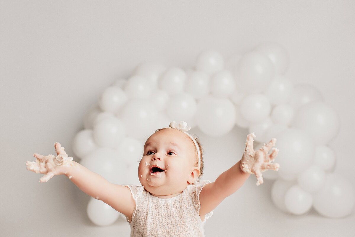  Baby smiling next to birthday cake during cake smash session