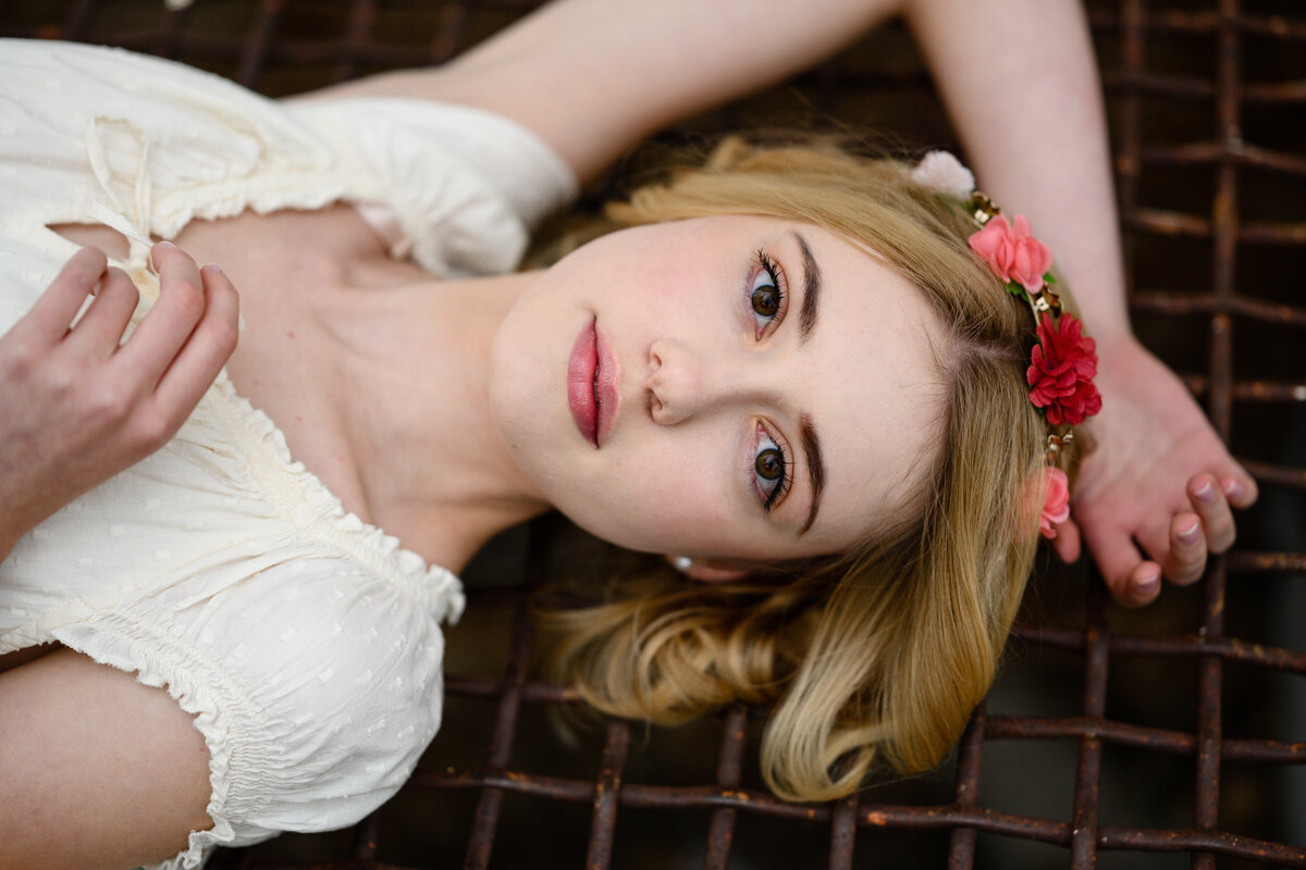 A denver senior photographer captures a denver senior girl laying on a metal grate with her hand above her head and a flower crown on her head