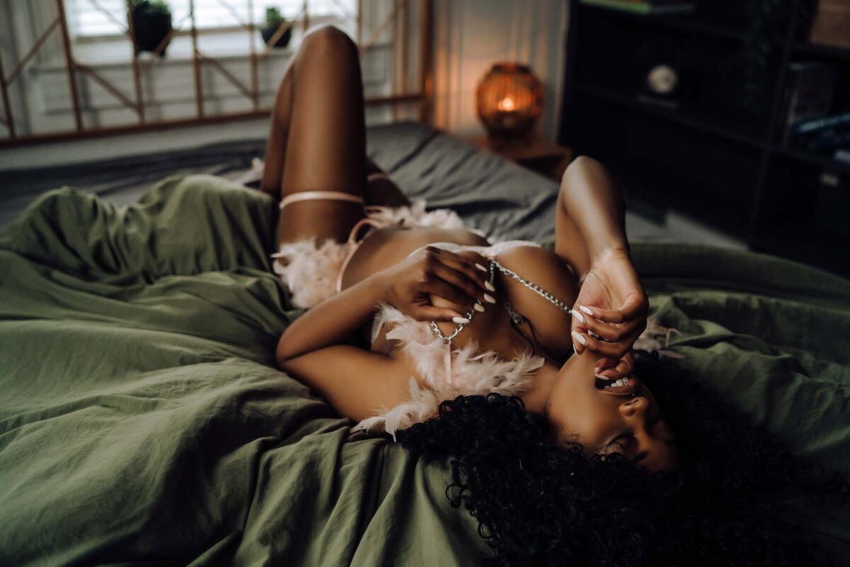 Dark skinned woman posing on sheets for boudoir photoshoot