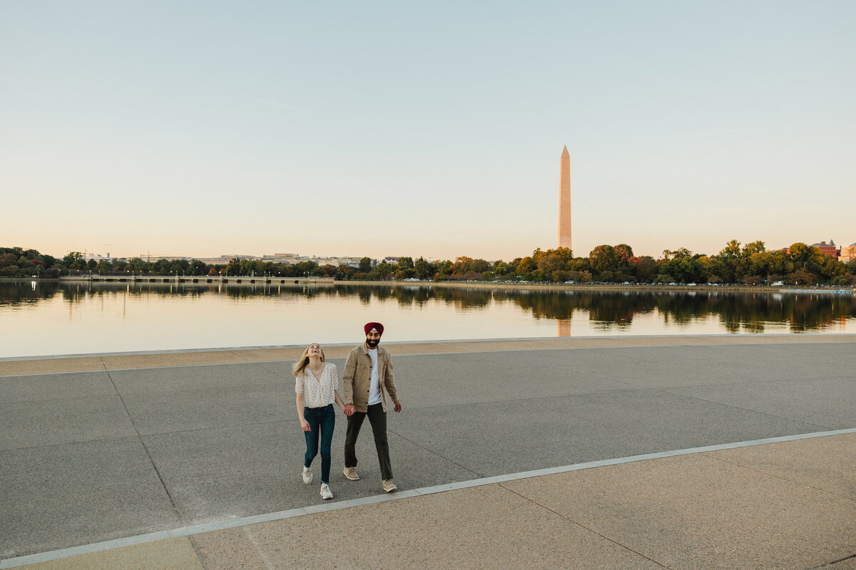 An engaged couple walks with views of DC behind them.