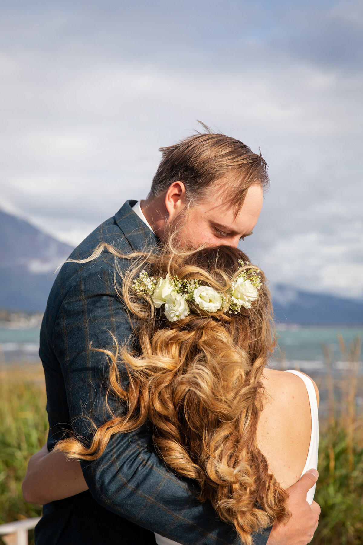 A groom kisses his bride's forehead as she leans in for a hug.