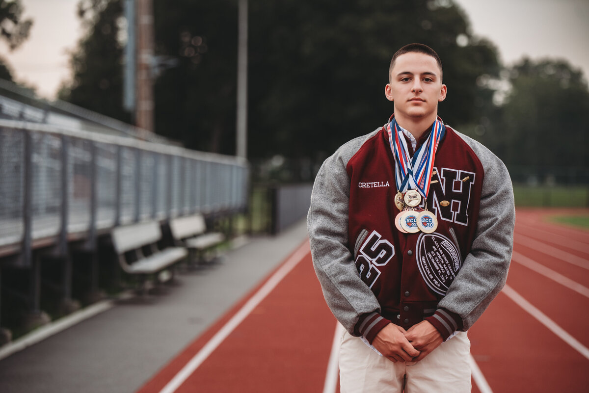 Showcase your high school achievements with a bold and dynamic senior portrait session in North Haven, CT. This athlete-inspired photoshoot highlights dedication, hard work, and school pride with a letterman jacket and championship medals on the track. Perfect for student-athletes looking to capture their senior year legacy. Book your session today!