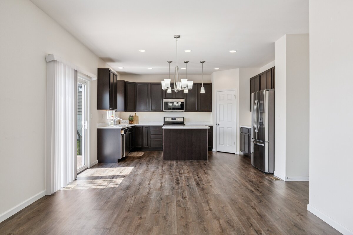 Real estate listing photograph of a kitchen with dark cabinets, white counters, and an island in the middle.