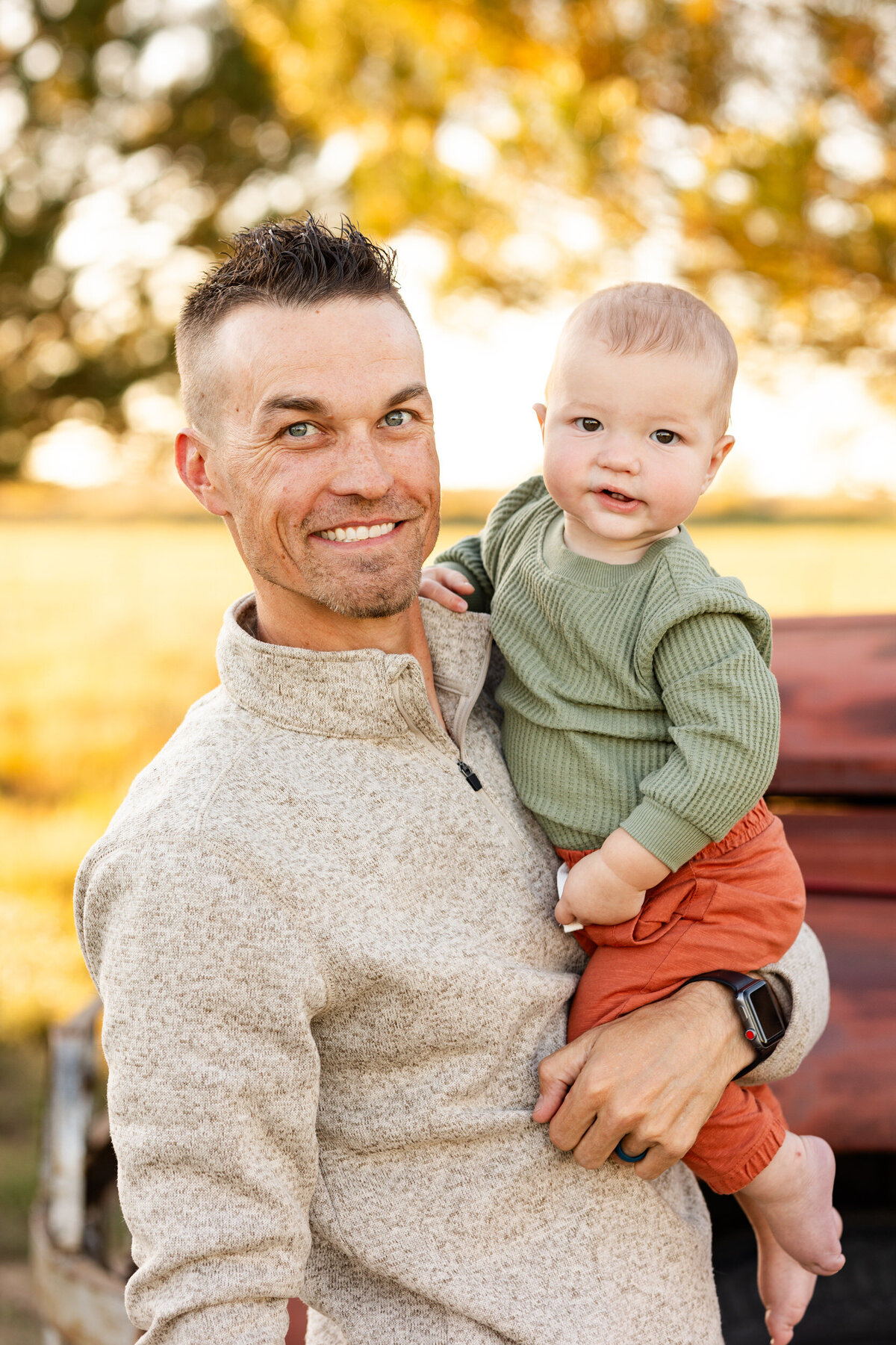 A dad holds his baby boy and they both smile at the camera.