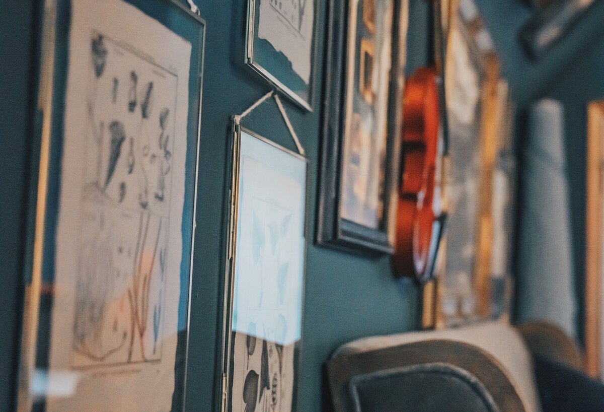Gallery wall with antique art prints and violing, with sofa bench and roll of upholstry fabric