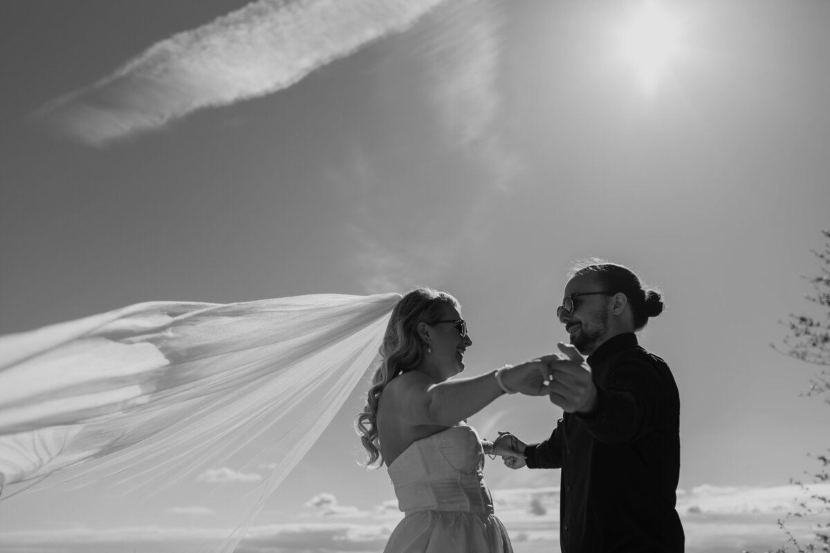 A black & white of the wind catching a bride’s veil during a cute moment with the groom. Captured by Fort Worth Wedding Photographer, Megan Christine Studio