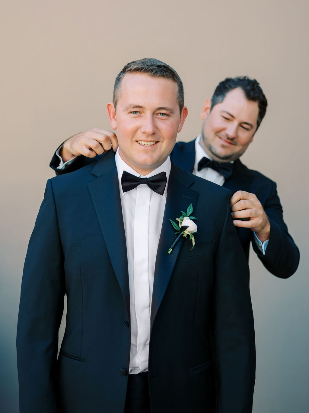 A groom shares a lighthearted moment while getting ready for the big day, dressed in a classic black tuxedo with a bow tie. Timeless wedding style and elegance.