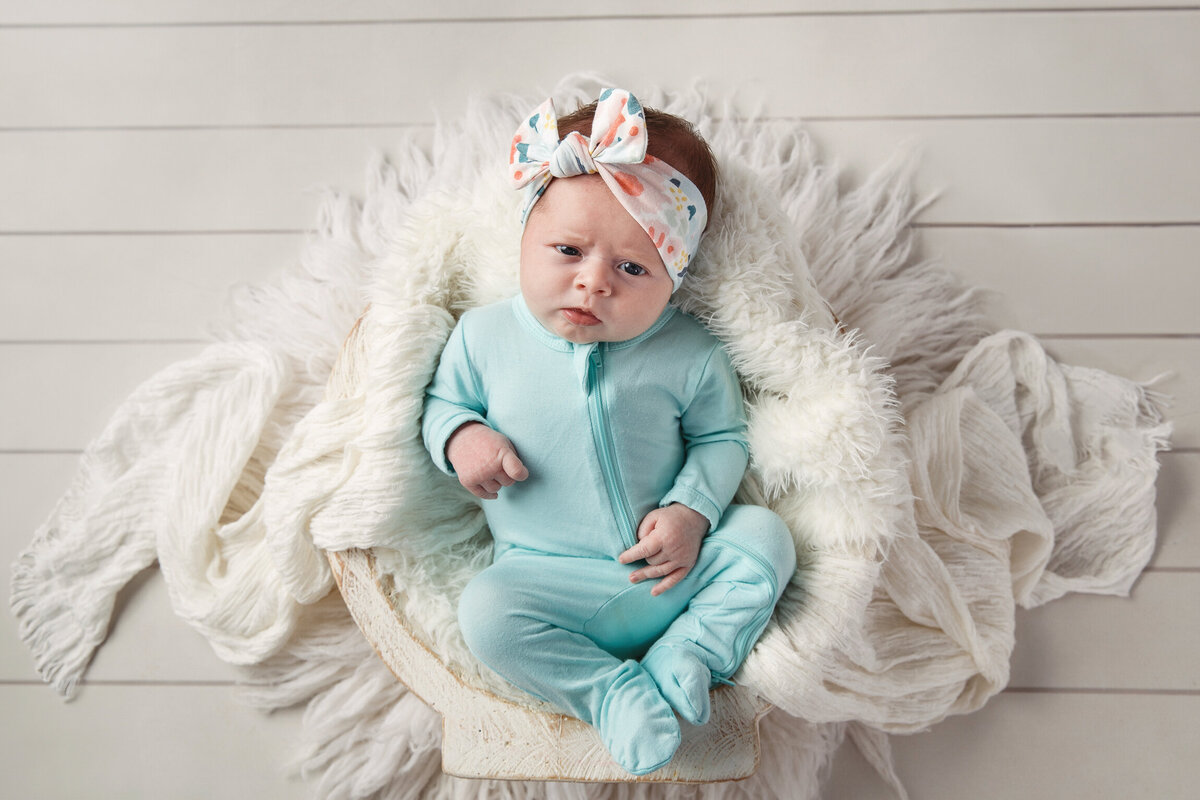 Pretty newborn photo of a baby girl wearing a blue jumper on a white background
