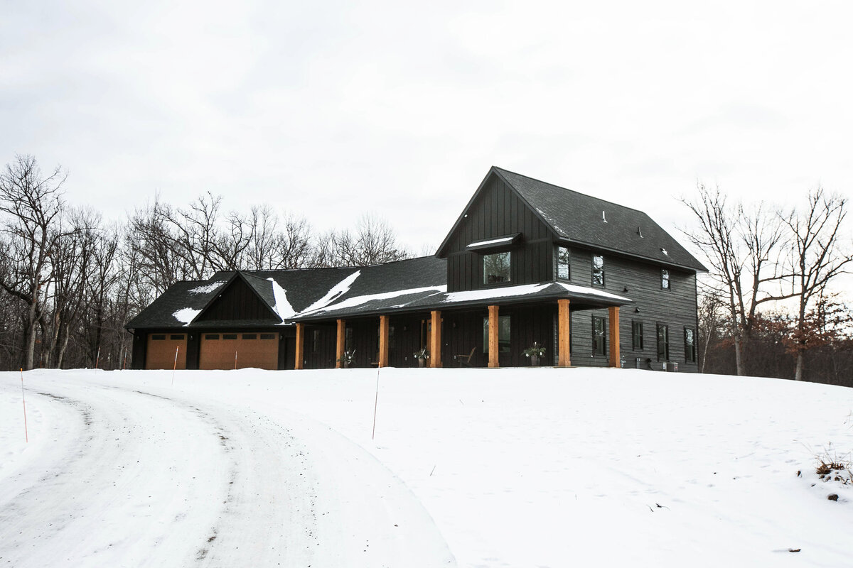 Exterior view of custom home in Elk River, Minnesota with black siding, wood details and front porch built by Cornerstone Custom Builds