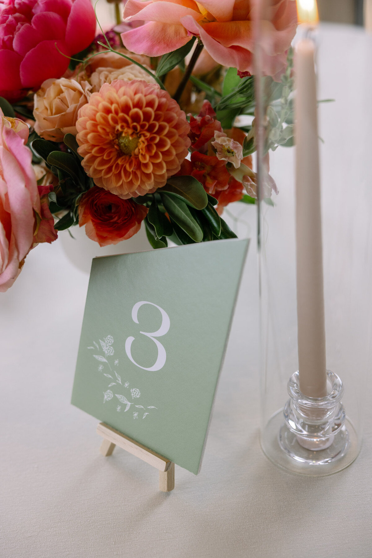 Angled wedding table numbers with custom calligraphy berry details at a wedding table with florals and pillar candles representing full service design and calligraphy by Life in Letters.