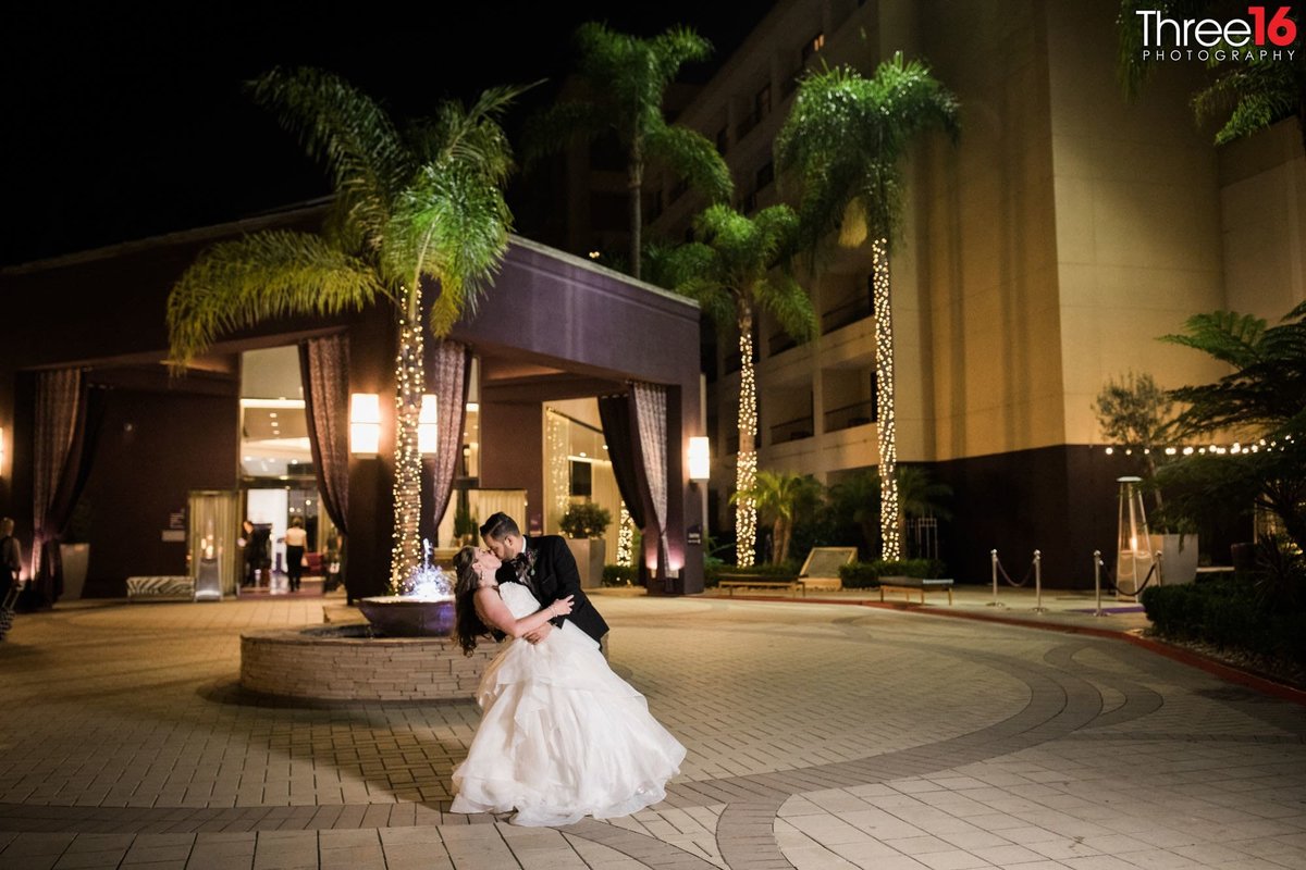 Groom dips his Bride and kisses her in front of the Avenue of the Arts Hotel in Costa Mesa, CA