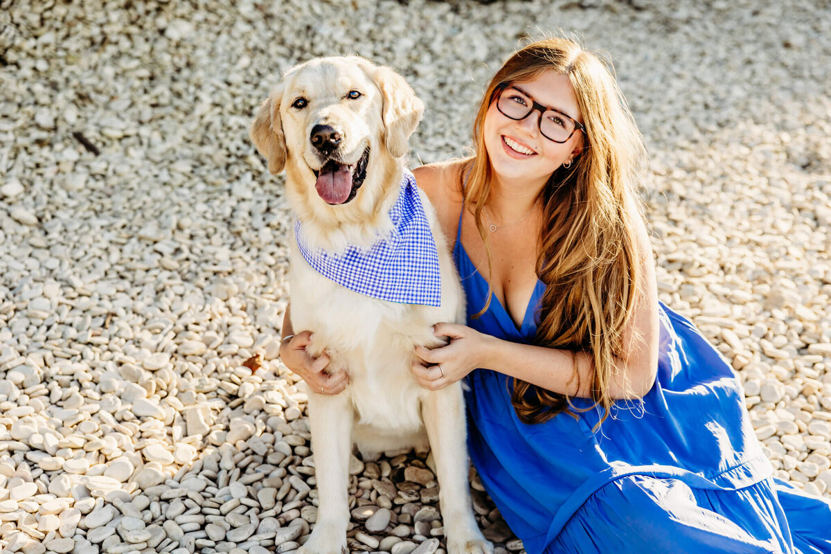 teenage girl in a bright blue dress snuggling her white lab that has a matching blue bandana on a beach near Oshkosh Wisconsin