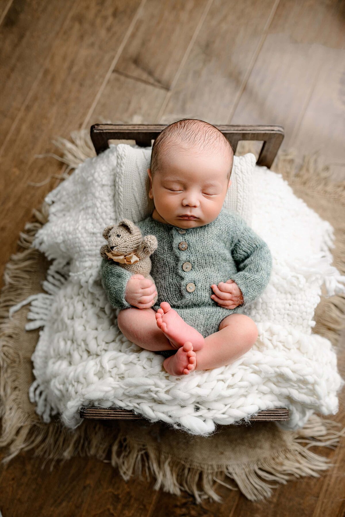 newborn dressed in a knit green outfit laying on a wooden bed