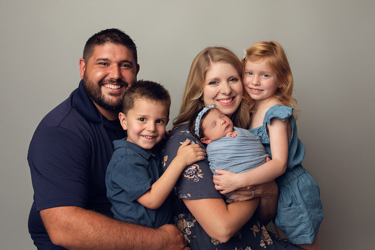 family of 5 holding newborn baby on a grey backdrop