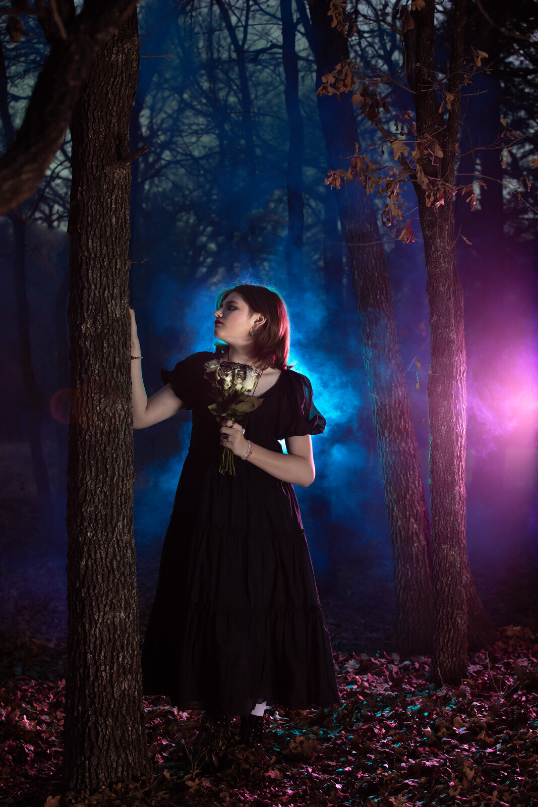 senior-girl-standing-by-tree-with-blue-and-purple-colored-lights-backlit