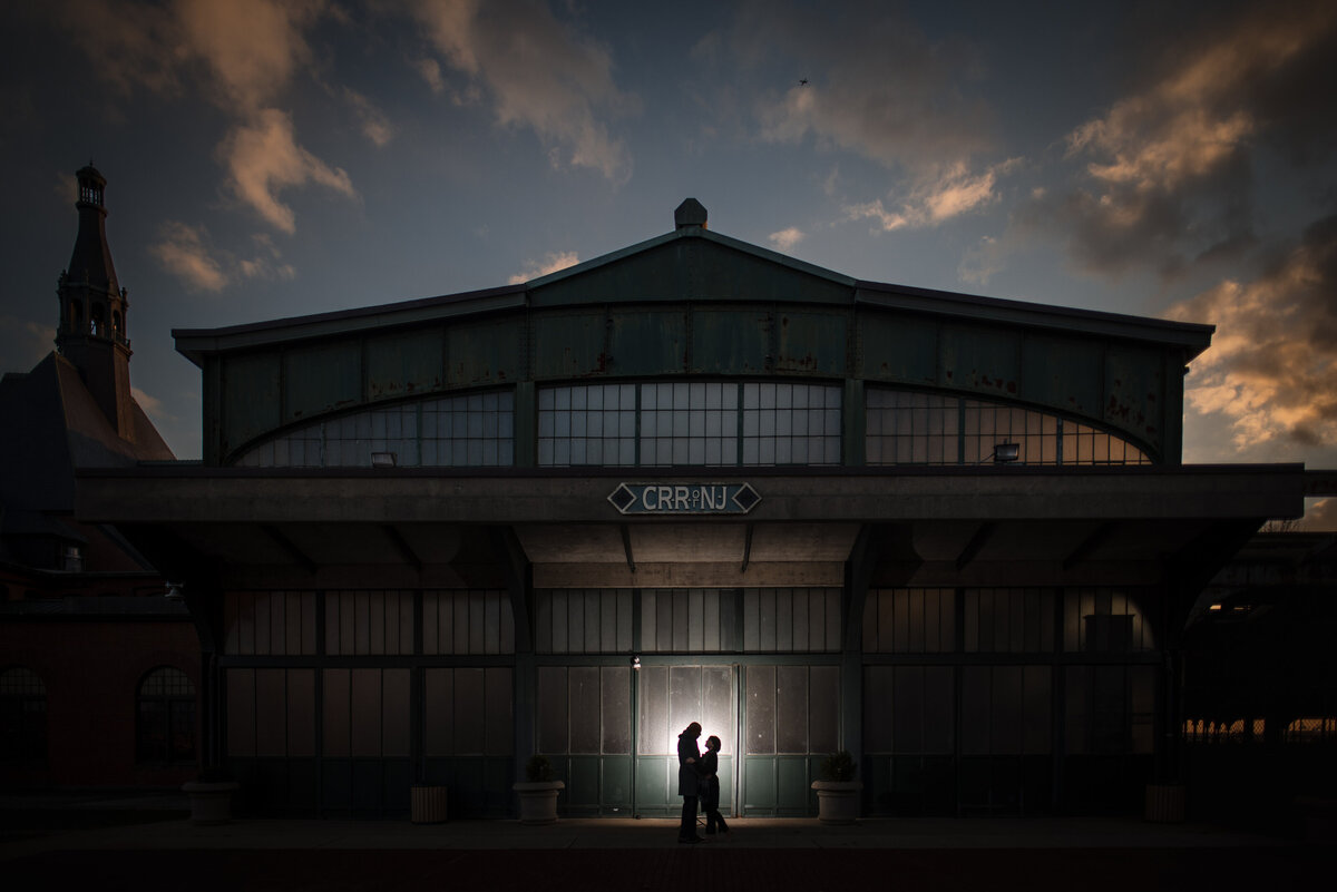 A couple standing in front of a large industrial building at sunset.