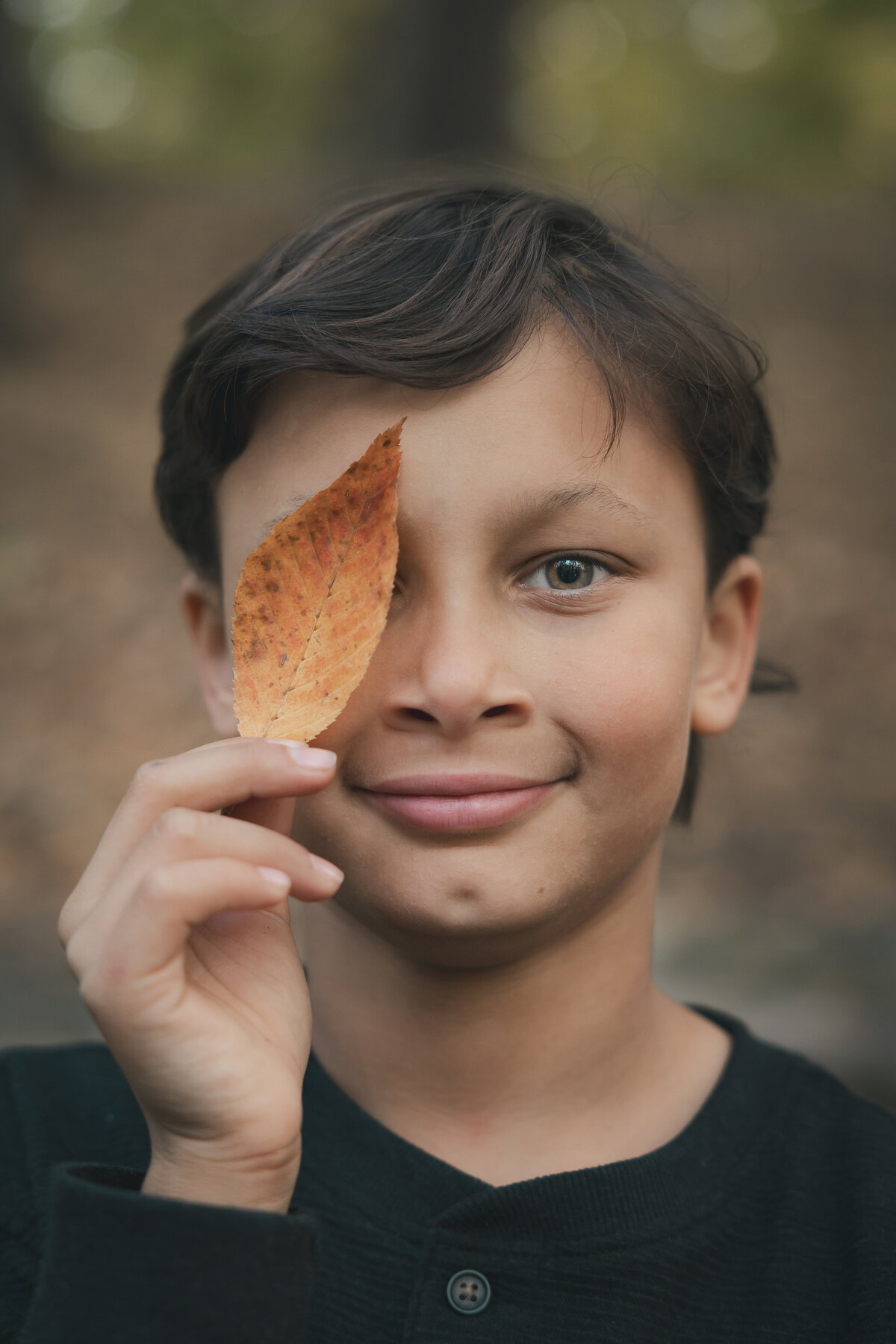 A fun photo of a handsome young boy holding a leaf over one of his eyes taken at Richfield Park, Davison MI
