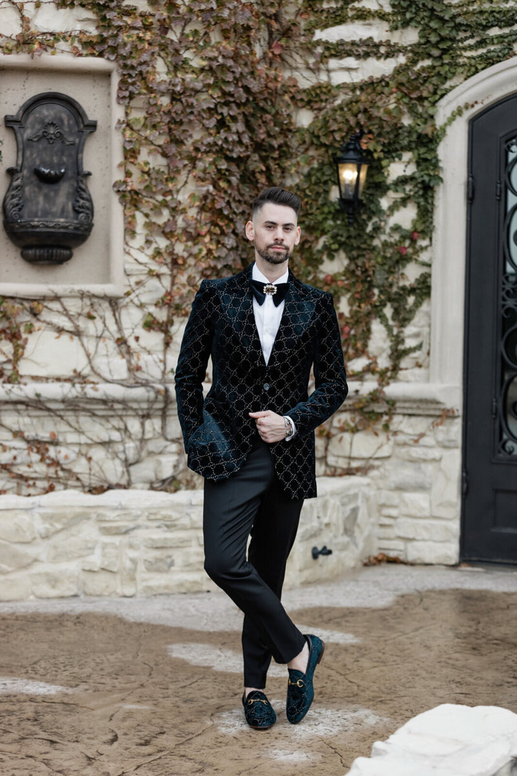 Portrait of a groom wearing Gucci, standing in front of a chateau wall covered in fall-colored vines.