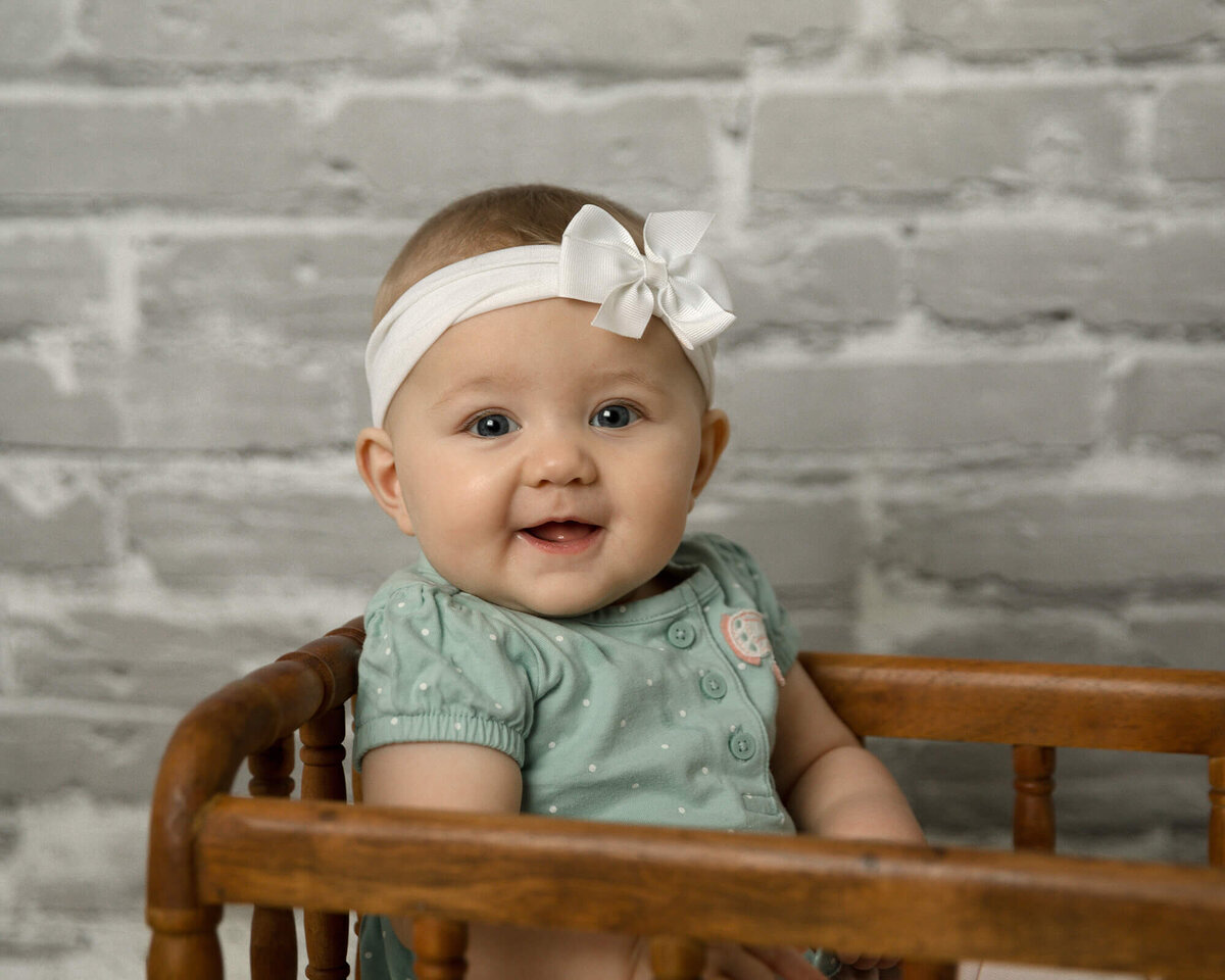 Baby girl sitting in a small wooden crib smiling.