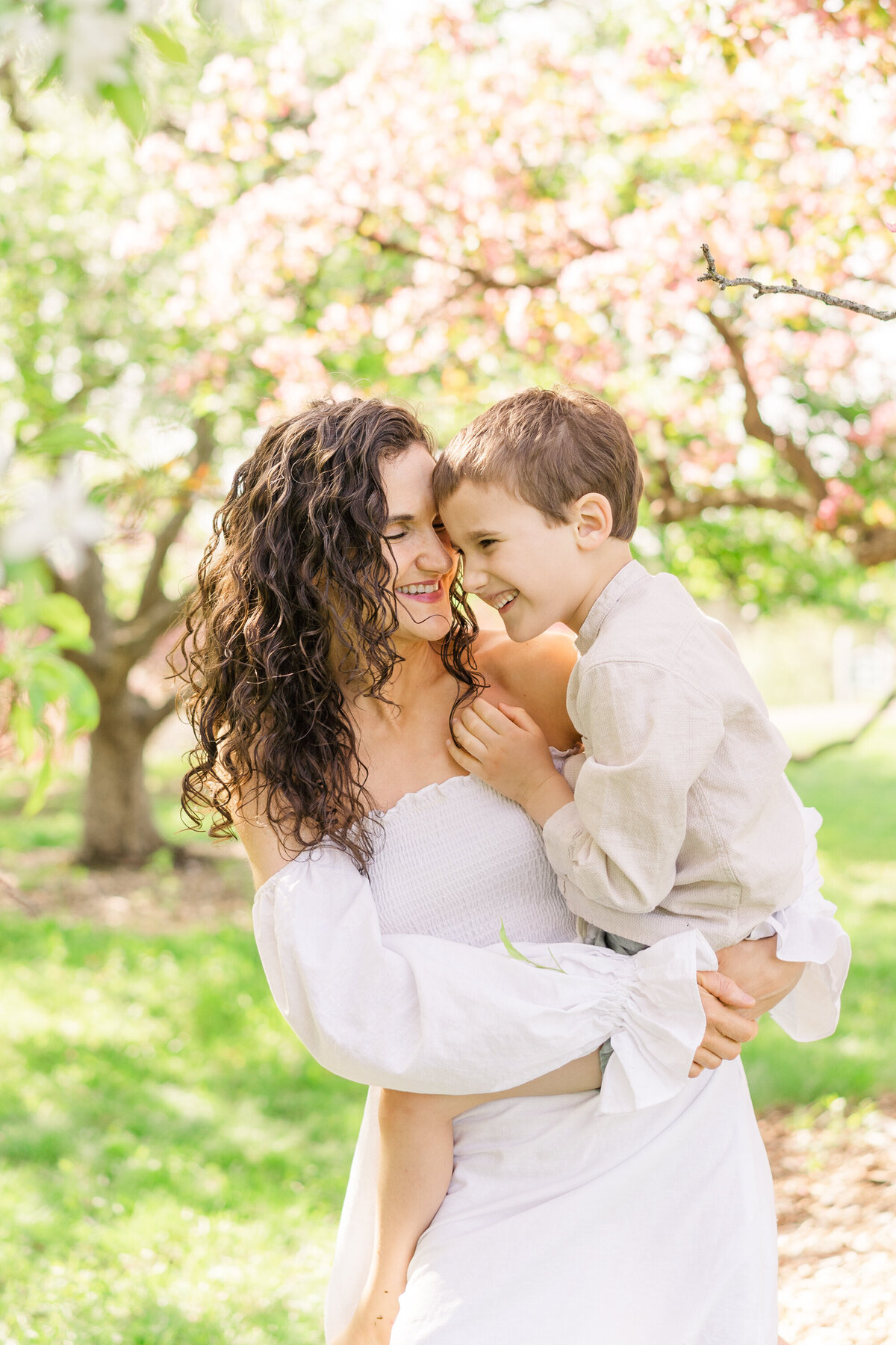 a mother holds her son in a  bright cherry blossom portrait session in the minneapolis area