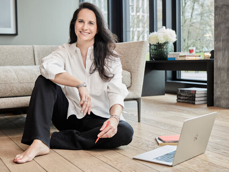 Silke, wellness coach for high-achieving women in midlife, smiling warmly while seated barefoot with a journal and laptop nearby.