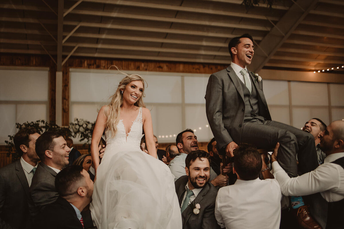 Wedding guests holding up newlyweds on chairs 