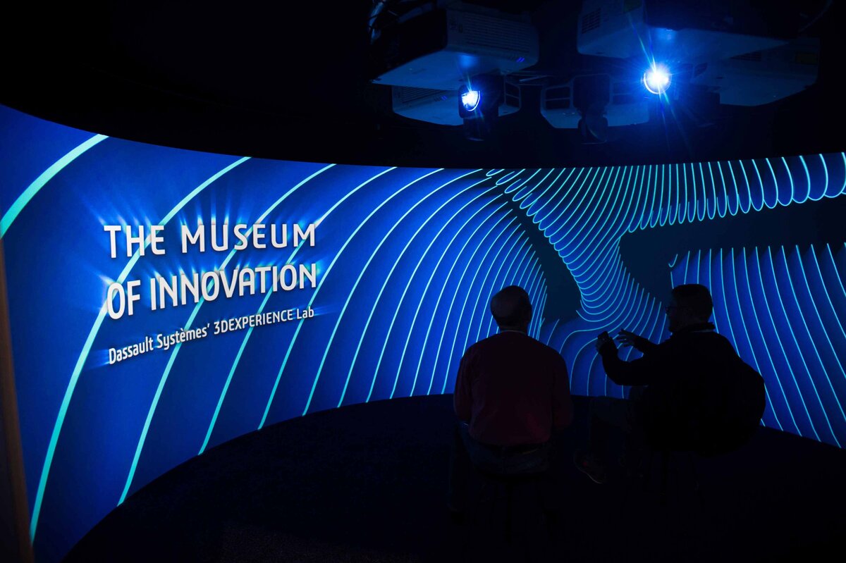 Interactive museum of innovation display with two people silhouetted on rounded screen in the dark