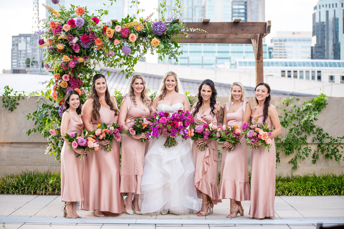 Vibrant bridesmaid bouquets accenting sunset color pallet with hues of lavender, orange, and golden yellow composed of petal heavy roses and ranunculus. Design by Rosemary and Finch in Nashville, TN.